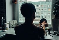 Image of a woman looking into a small mirror in a dark room.
