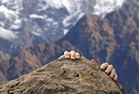 A mans hands are seen grasping the edge of a cliff.