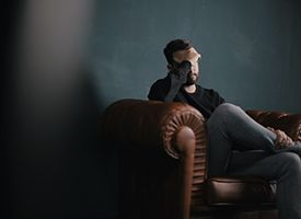 A disappointed man sitting in a dark room on a couch.