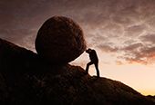 Silhouette of young businessman pushing large stone uphill.