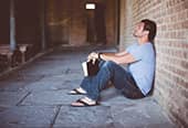 Distressed man sitting against a brick wall, holding the bible in his hands