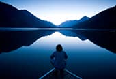 A man sits at the front of a boat on a calm lake