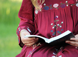 Woman in red floral dress reading a spanish copy of the Book of Mormon outside..