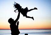 Silhouette of a young girl being tossed into the air by her father.