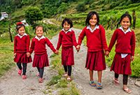 5 young Nepalese girls wearing red hold hands and walk down a gravel road