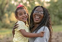 A woman laughs with her child at sunset.
