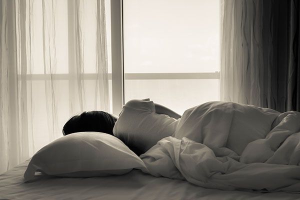 Young woman lying in bed, looking towards through the window - black and white photo.